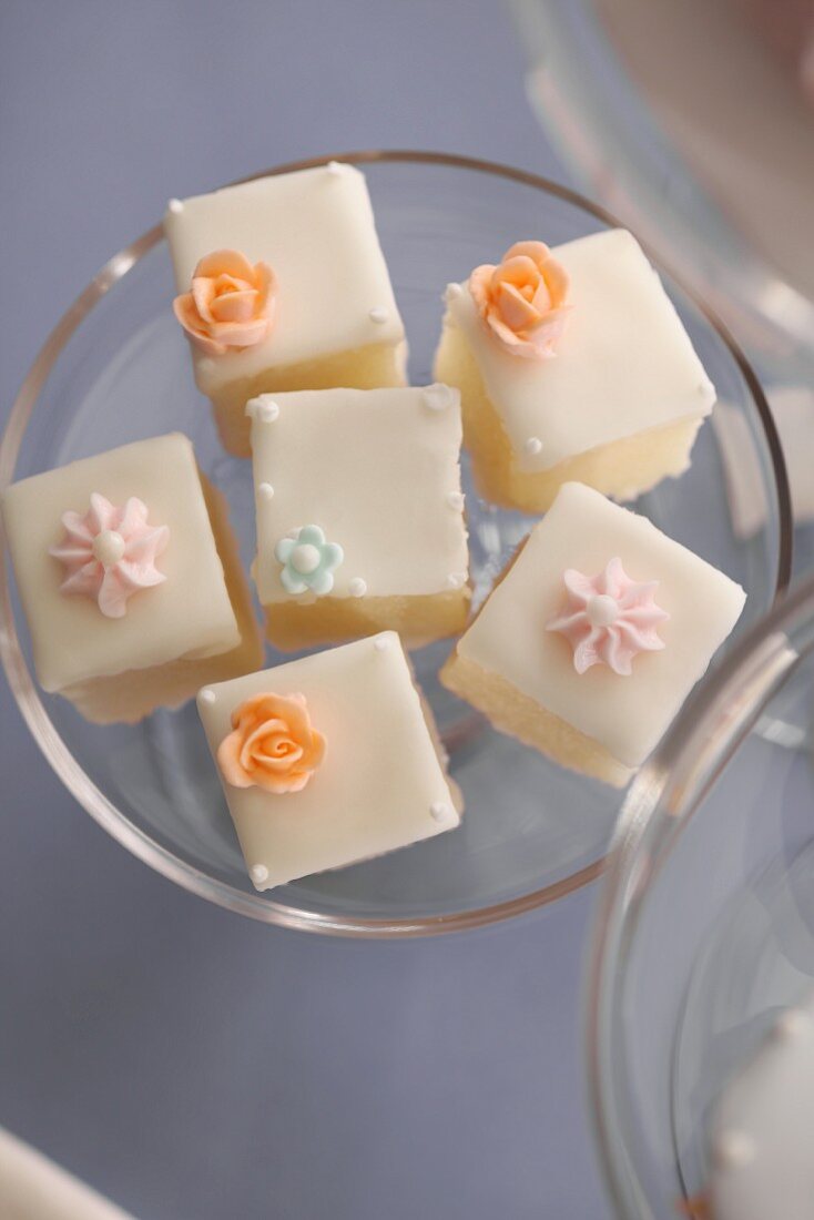 Mehrere Petit Fours mit Zuckerblüten auf Kuchenständer