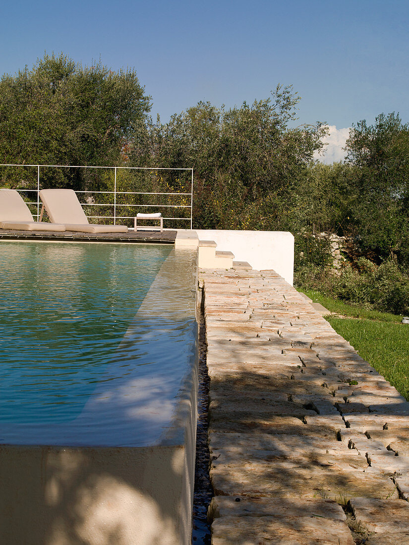 Pool with overflow and stone-flagged path in Mediterranean garden