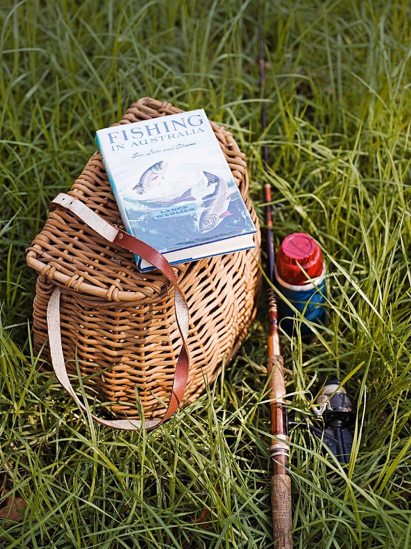 A fisherman's basket, a book and a fishing rod in field
