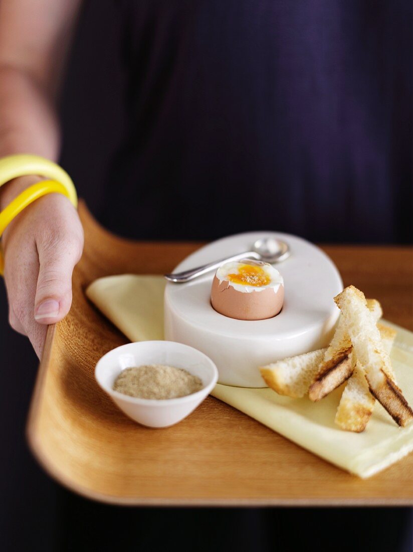 A woman holding a tray with a boiled egg and soldiers