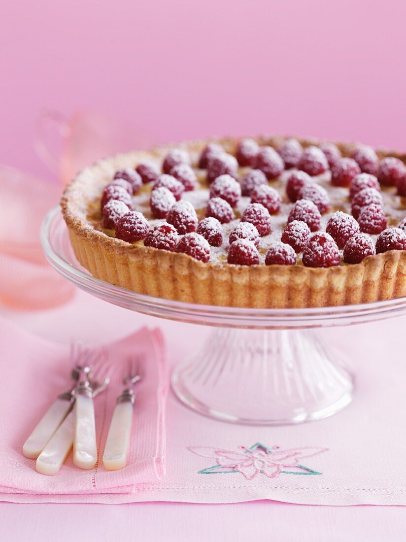 Raspberry tart with icing sugar on a cake stand