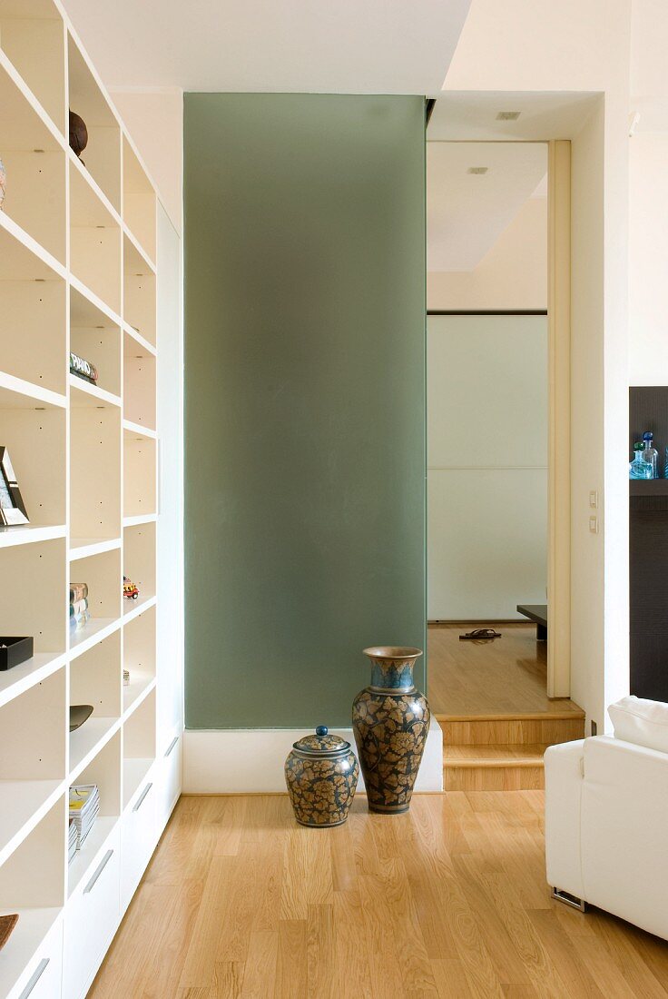 Corner of modern living room - Chinese vases against glass wall next to doorway and modern, white fitted shelving