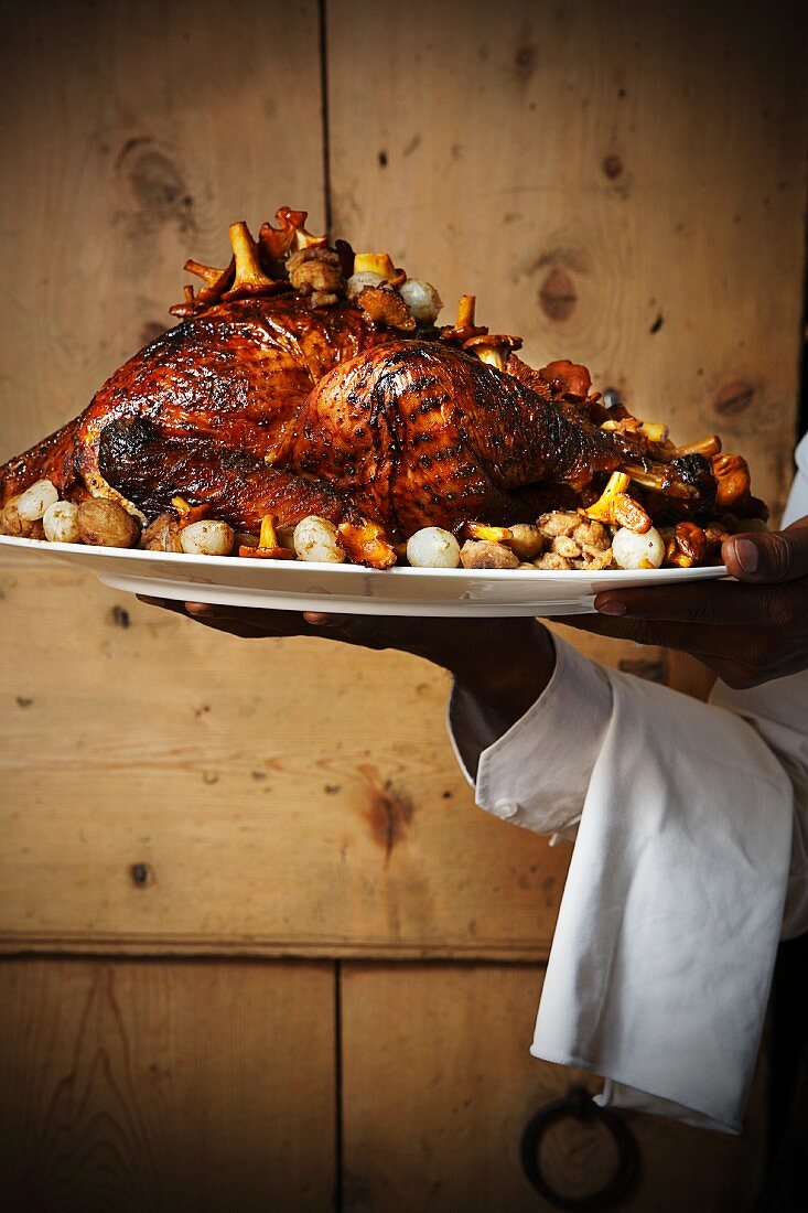 A waiter serving roast turkey with chanterelle mushrooms and onions