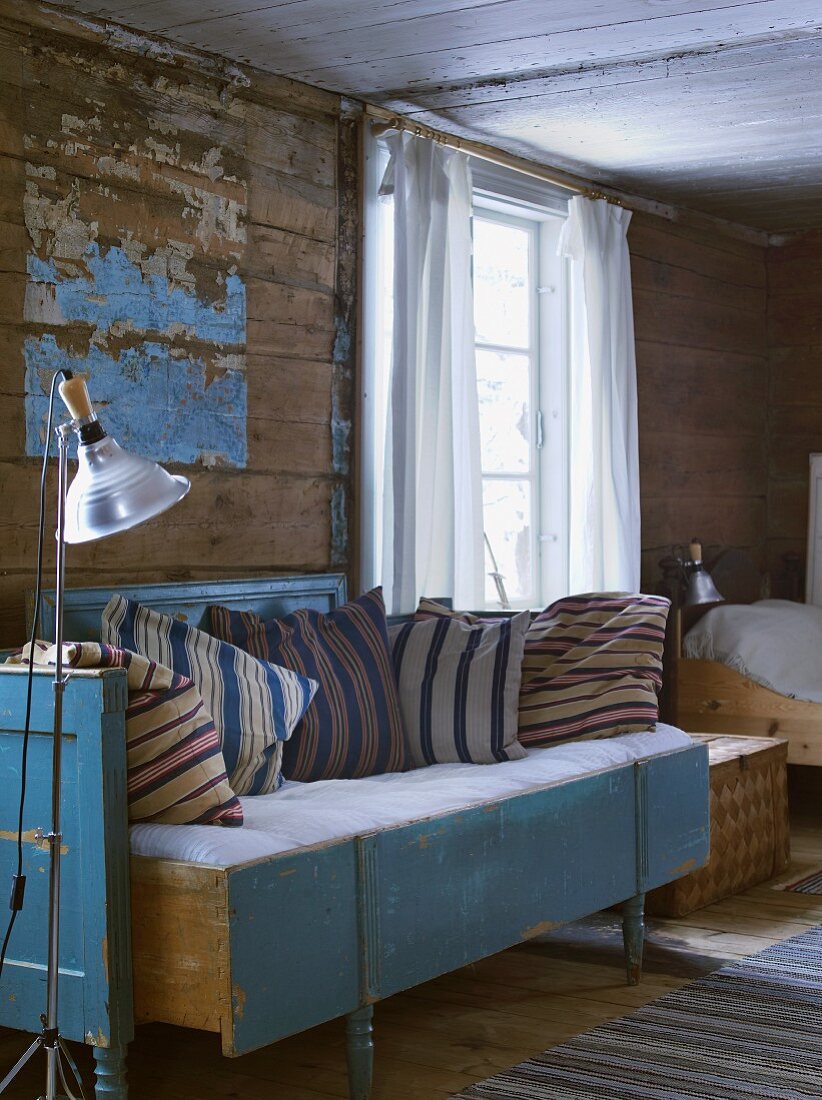 Cushions on rustic sofa against wooden wall with peeling paint