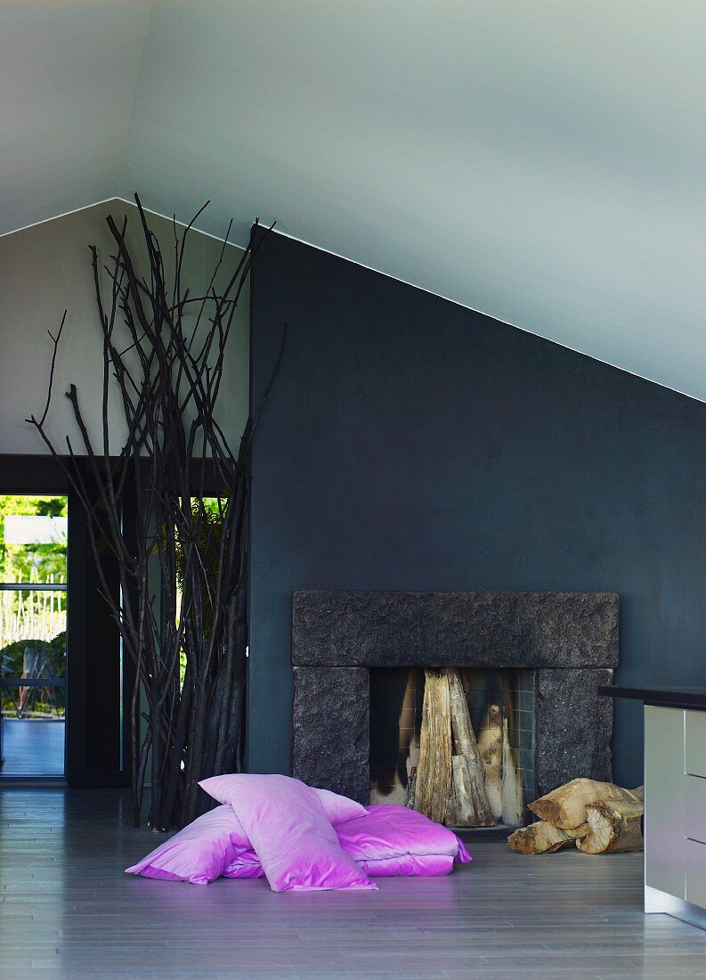 Pink cushions on floor in front of open fireplace and black-painted wall