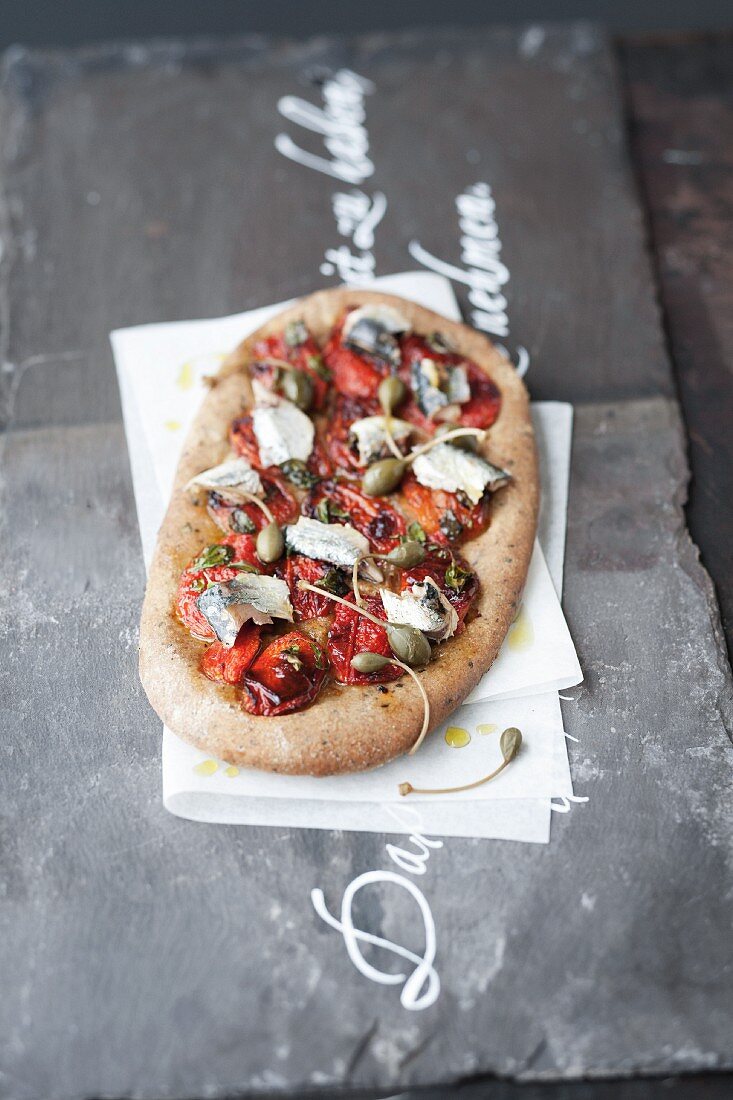 A pizza topped with oven-baked tomatoes and sardines