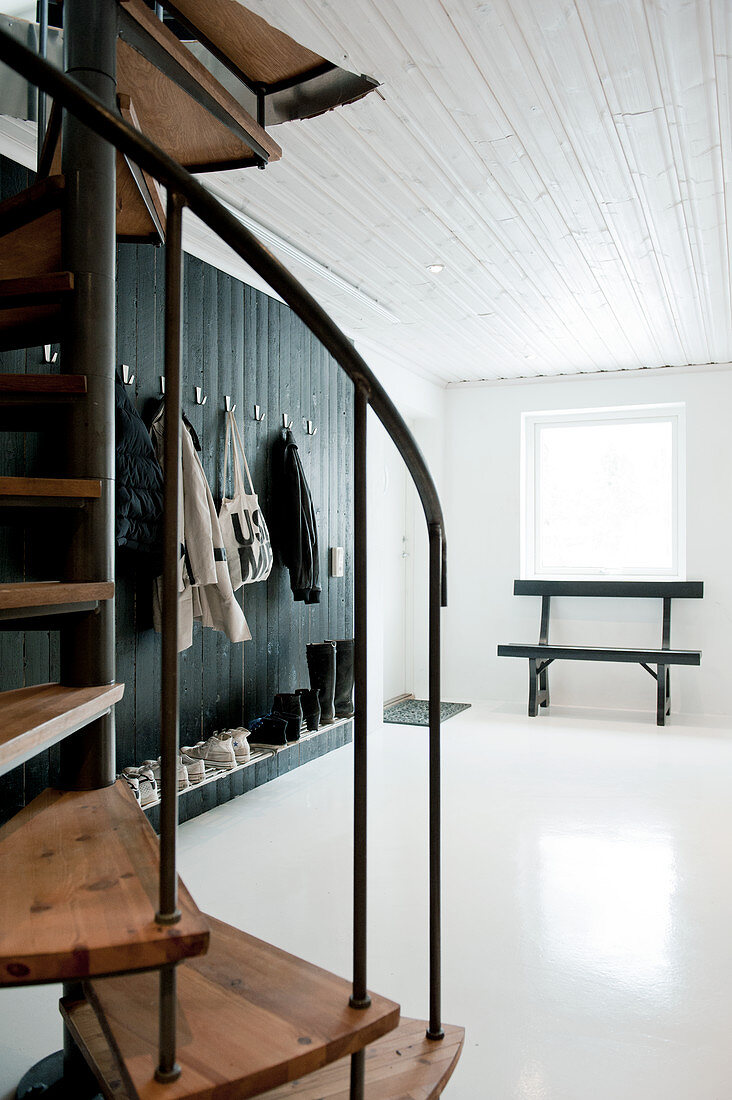 Black and white cloakroom in foyer with painted wood panelling and spiral staircase in foreground