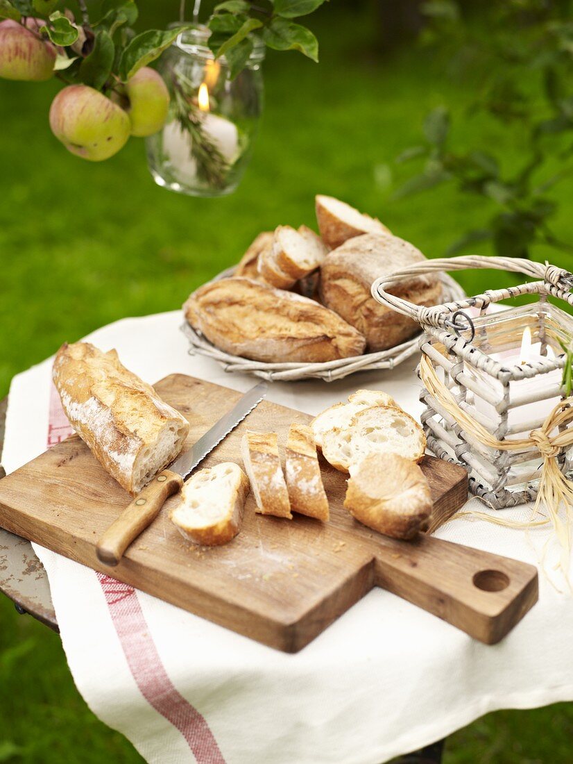 Baguette auf Scheindebrett und andere Brote im Brotkorb auf einem Tisch im Freien