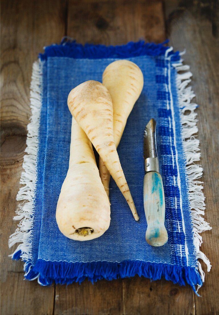 Three parsnips on a cloth with a peeler