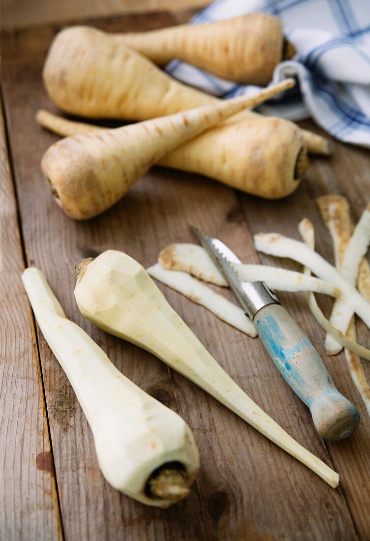 Parsnips, some peeled, on a wooden surface