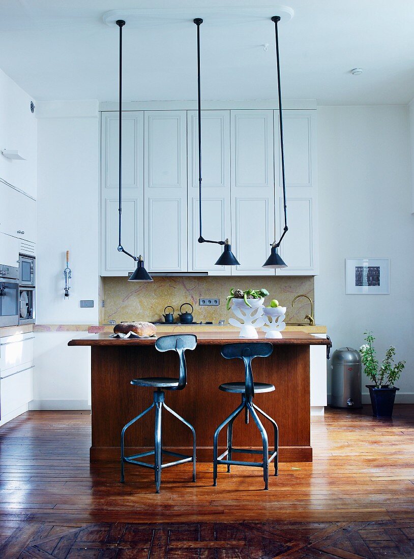 Vintage pendant lamps above wooden counter and bar stools in open-plan kitchen