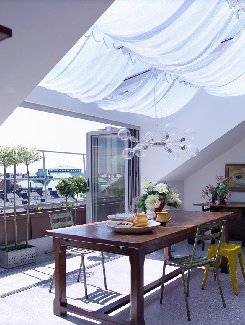 Dining area below skylight with awning in front of open, folding terrace doors