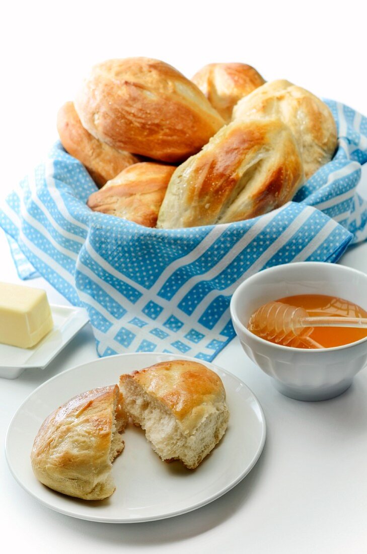 Basket of Bolillo Rolls; One on a Plate Halved; Honey in a Bowl