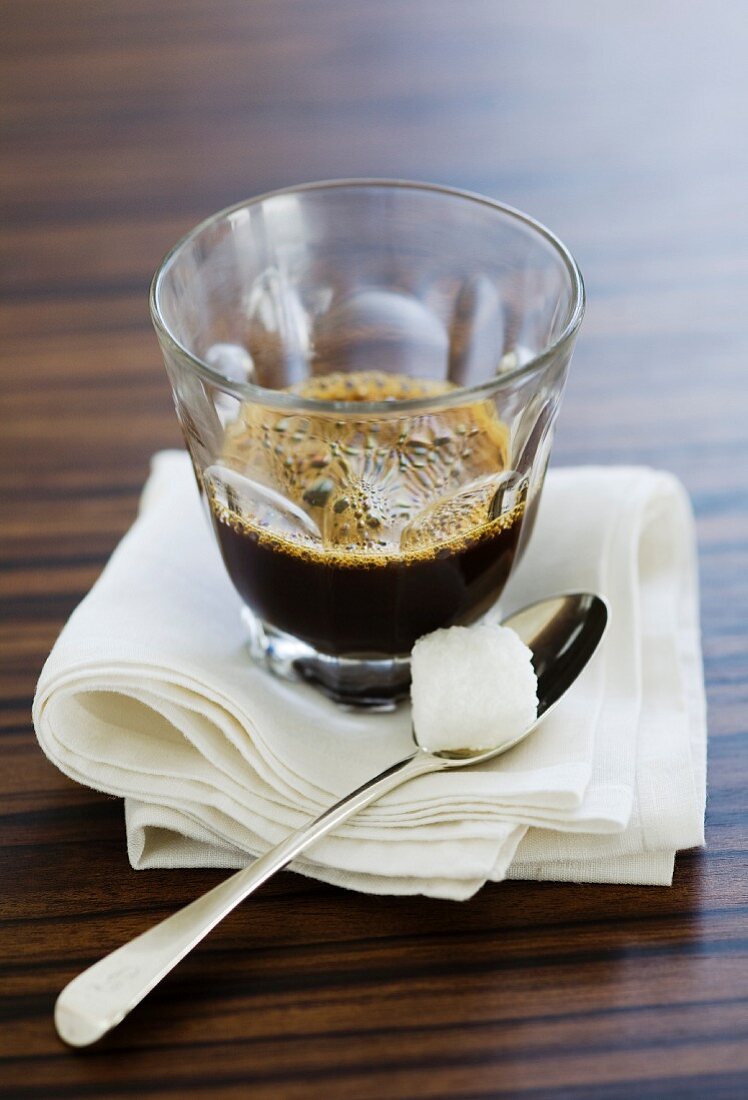 A glass of espresso with a lump of sugar