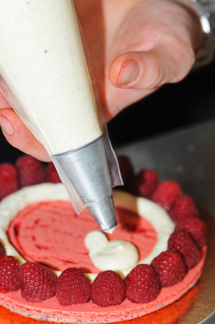 A raspberry tartlet being decorated with cream from a piping bag
