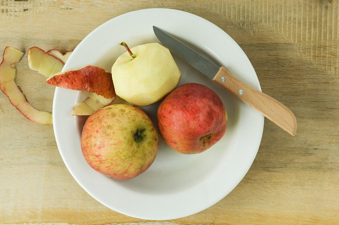 Organic apples, whole and peeled, on a plate with a knife