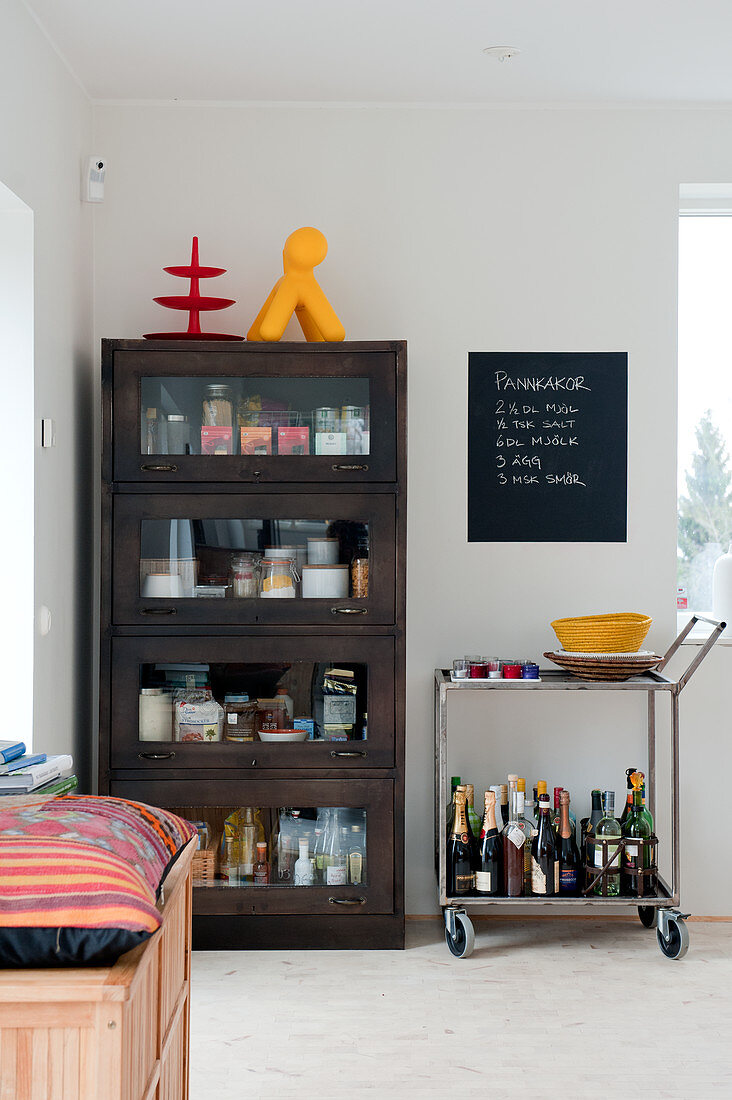 Dark wood display case next to portable bar on tea trolley in corner of modern dining room