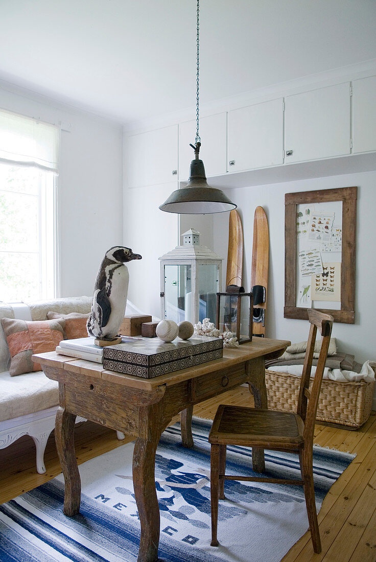 Massivholztisch und Stuhl auf weiss-blau gemustertem Teppichläufer in ländlichem Wohnzimmer mit Vintage Hängeleuchte und ausgestopftem Pinguin