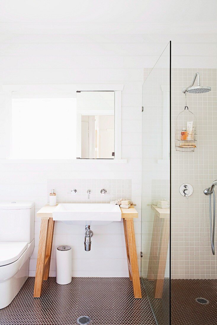 Free standing vanity with wall faucet and mirror next to a shower partition