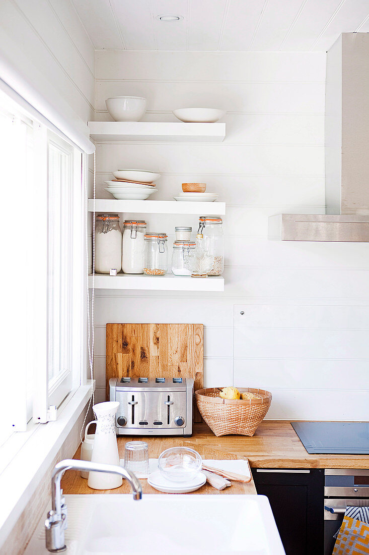 White sink, wooden worksurface and white wall-mounted shelves in kitchen