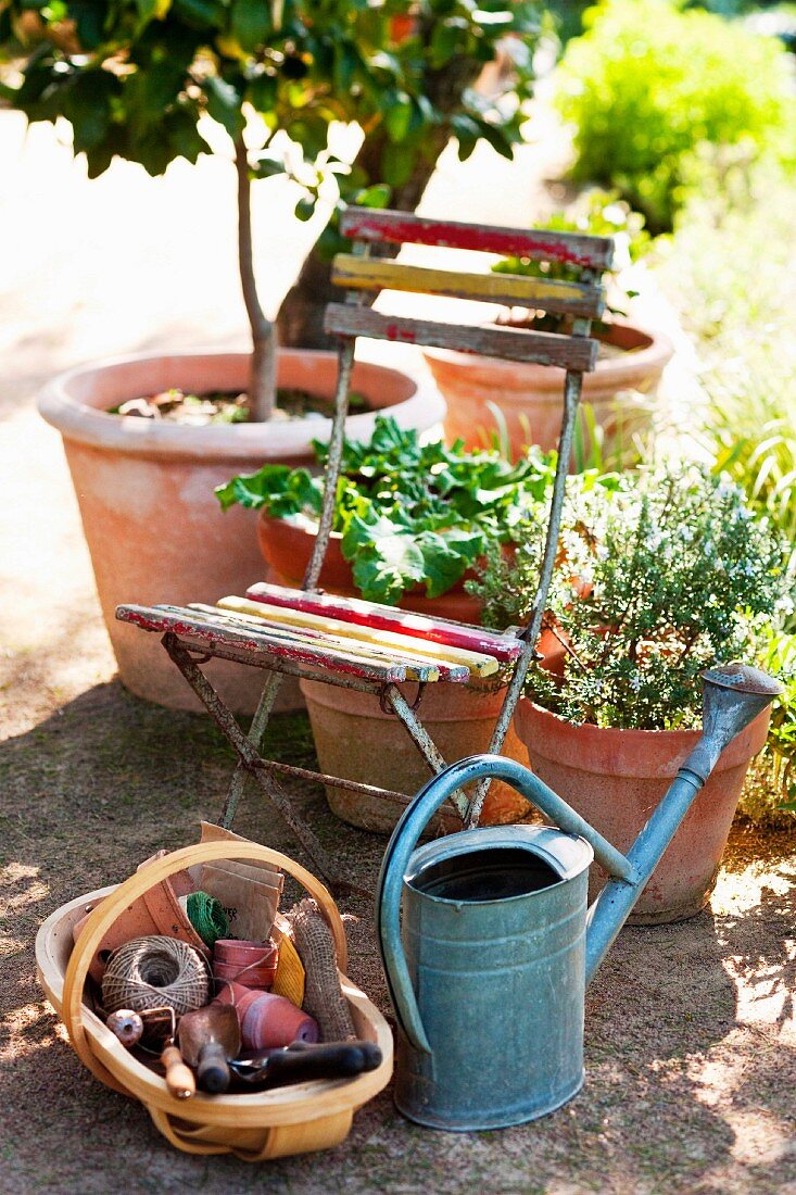 Old folding chair in the garden next to a metal watering can and basket with craft supplies