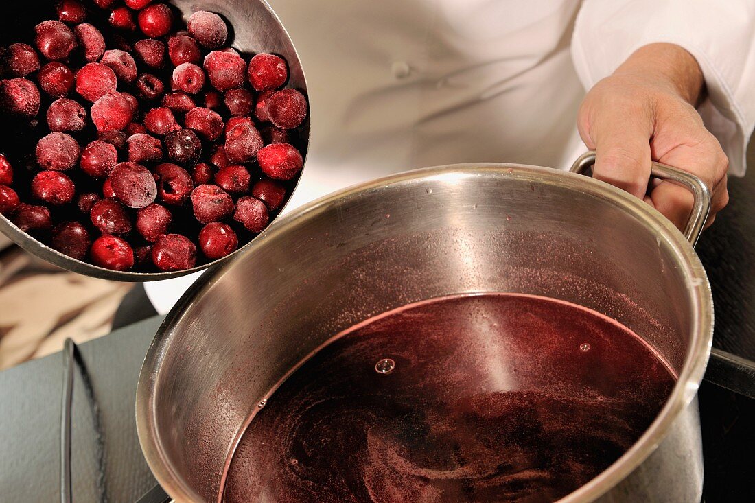 Morello cherries being put in a pot of red wine sauce