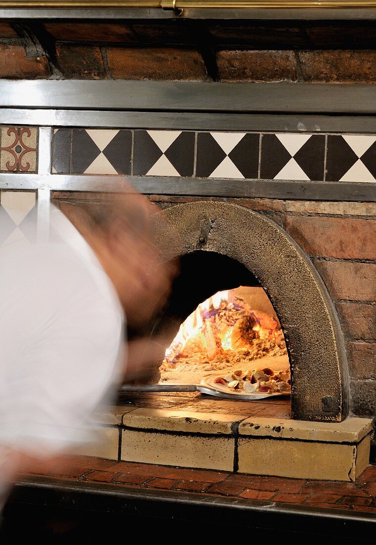 Pizzabäcker schiebt Pizza in den Steinofen