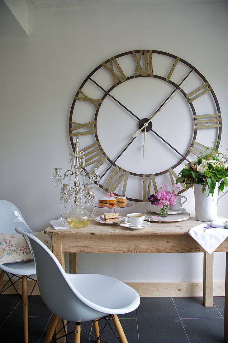 Holztisch mit weissen Schalenstühlen und grosse Wanduhr in einer Küche