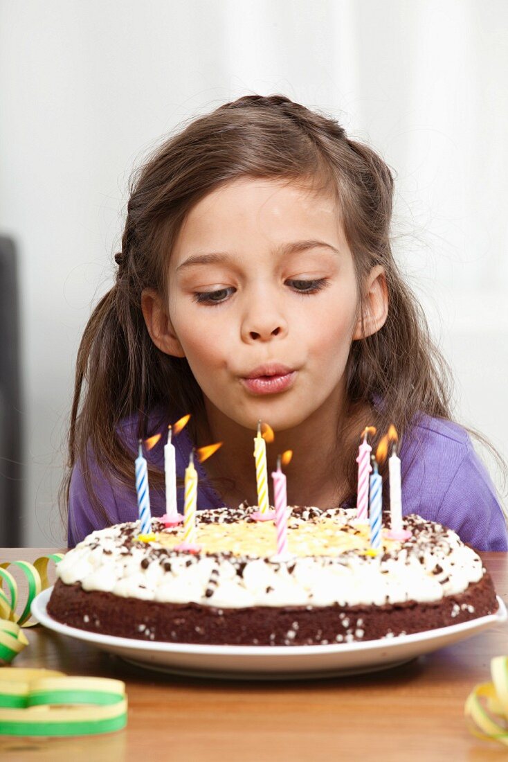 Mädchen bläst Kerzen auf Geburtstagstorte aus