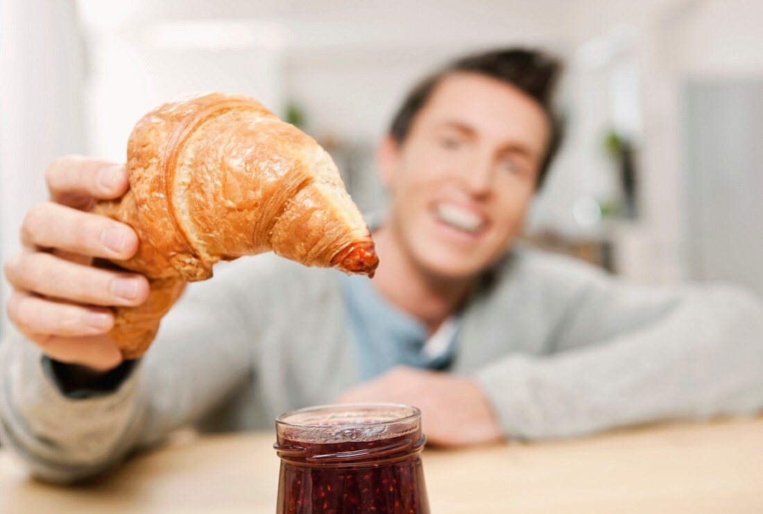 A man eating a croissant with jam