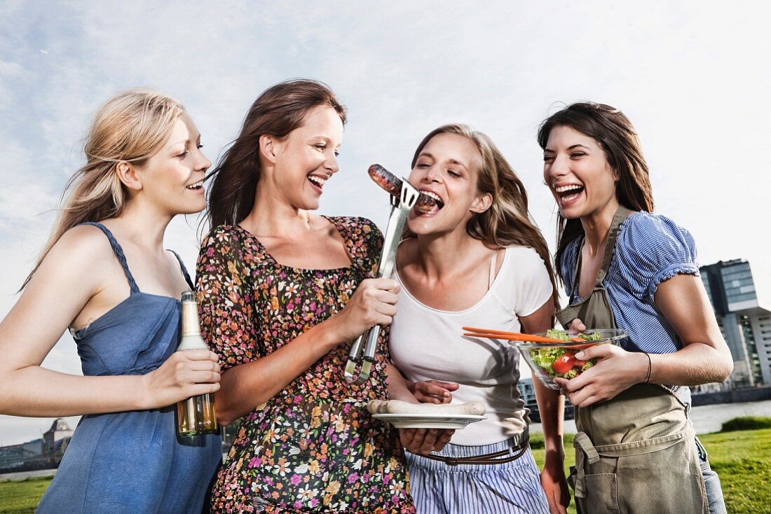 Junge Frauen essen Grillwürstchen am Flussufer