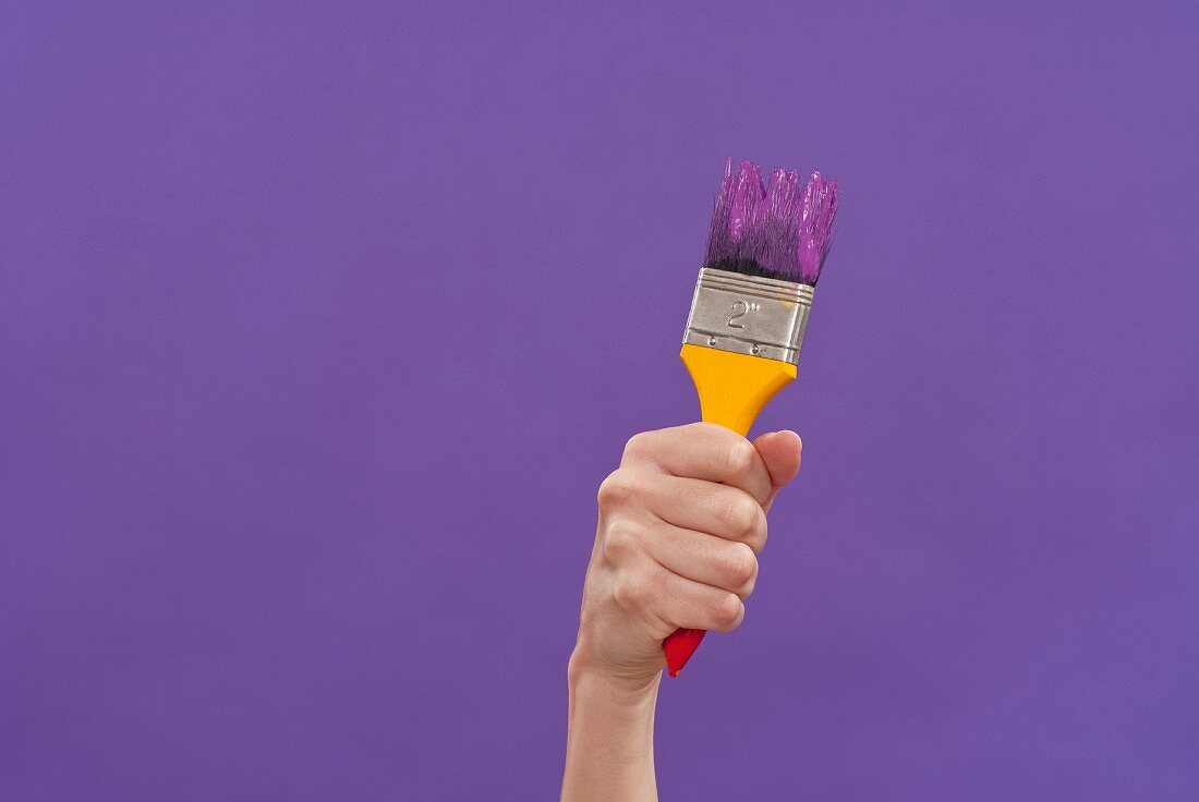 Hand hält Pinsel mit lila Farbe