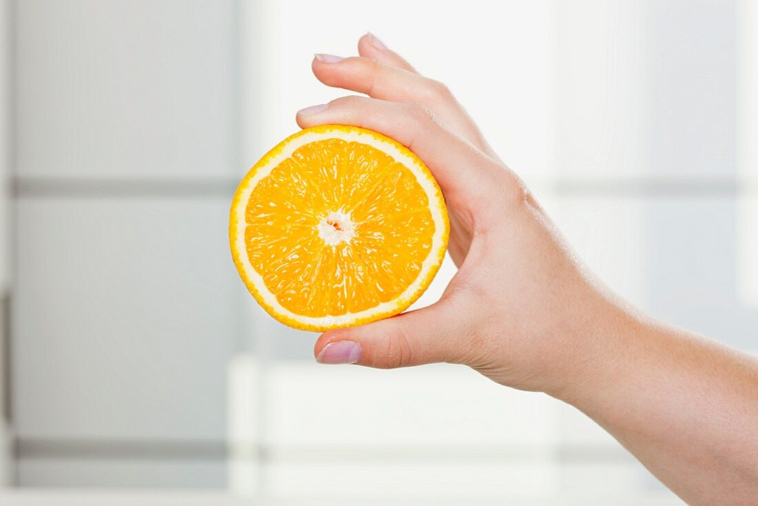 Hand hält eine Orangenhälfte