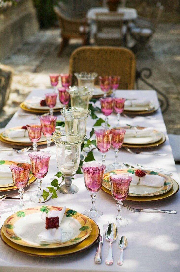 Festlich gedeckter Tisch in Freiem mit farbigen Weingläsern und Teller mit Blumenmotiven auf weisser Tischdecke