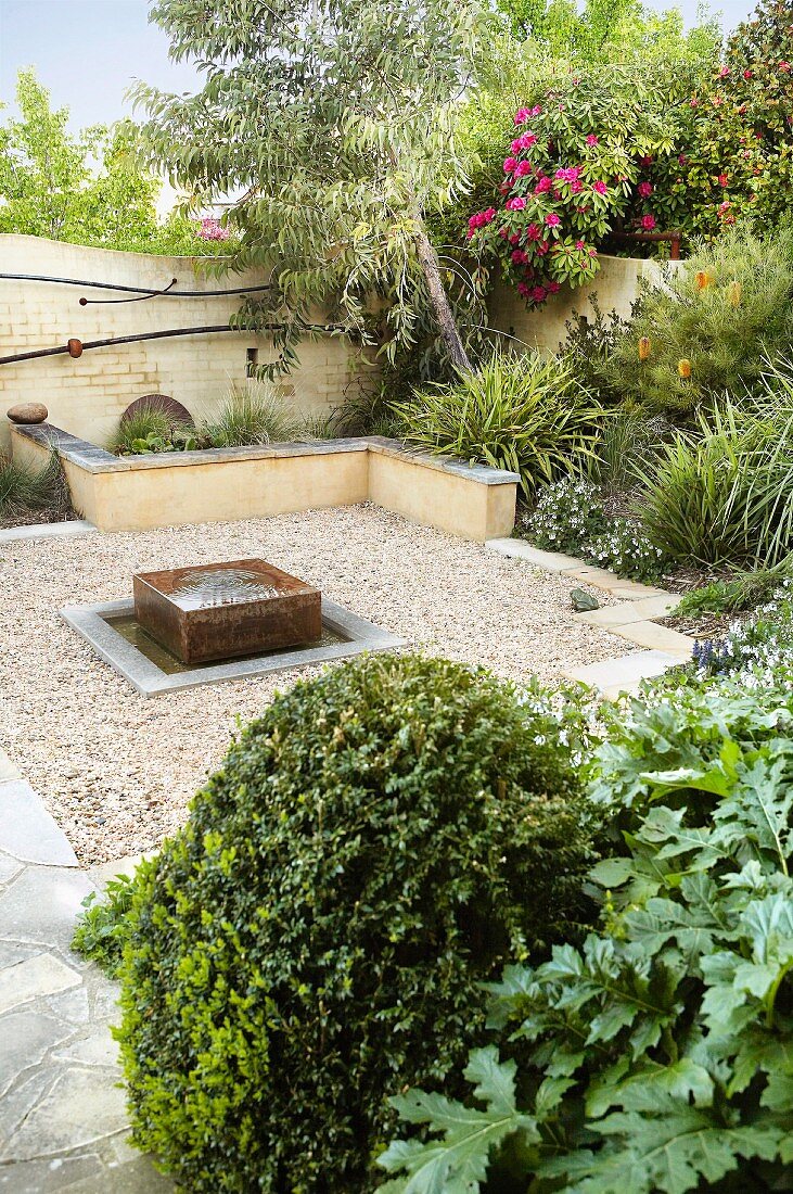 Relaxation area in lushly planted gravel garden with modern fountain