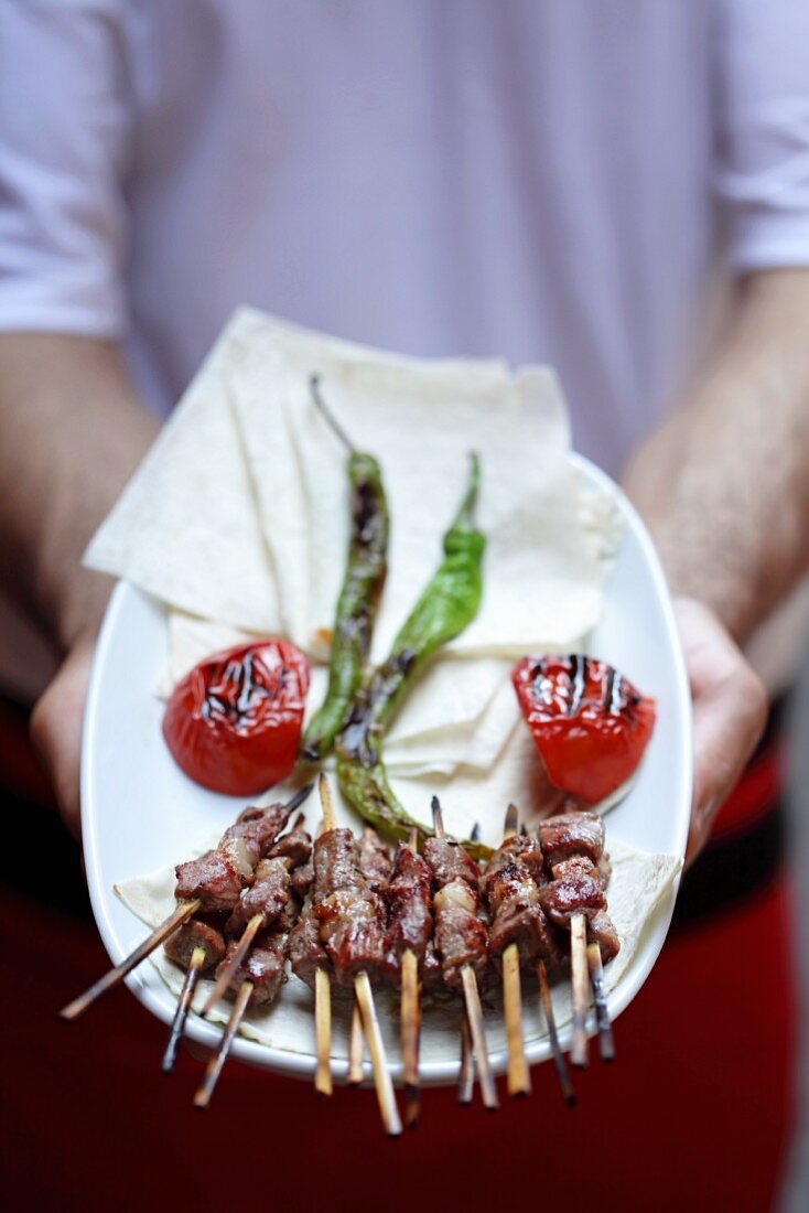 Mann serviert Spiesschen mit Grillgemüse