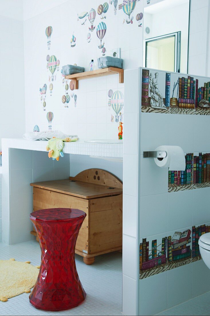 Modern bathroom with red stool in front of masonry washstand against white-tiled wall with hot-air balloon motifs