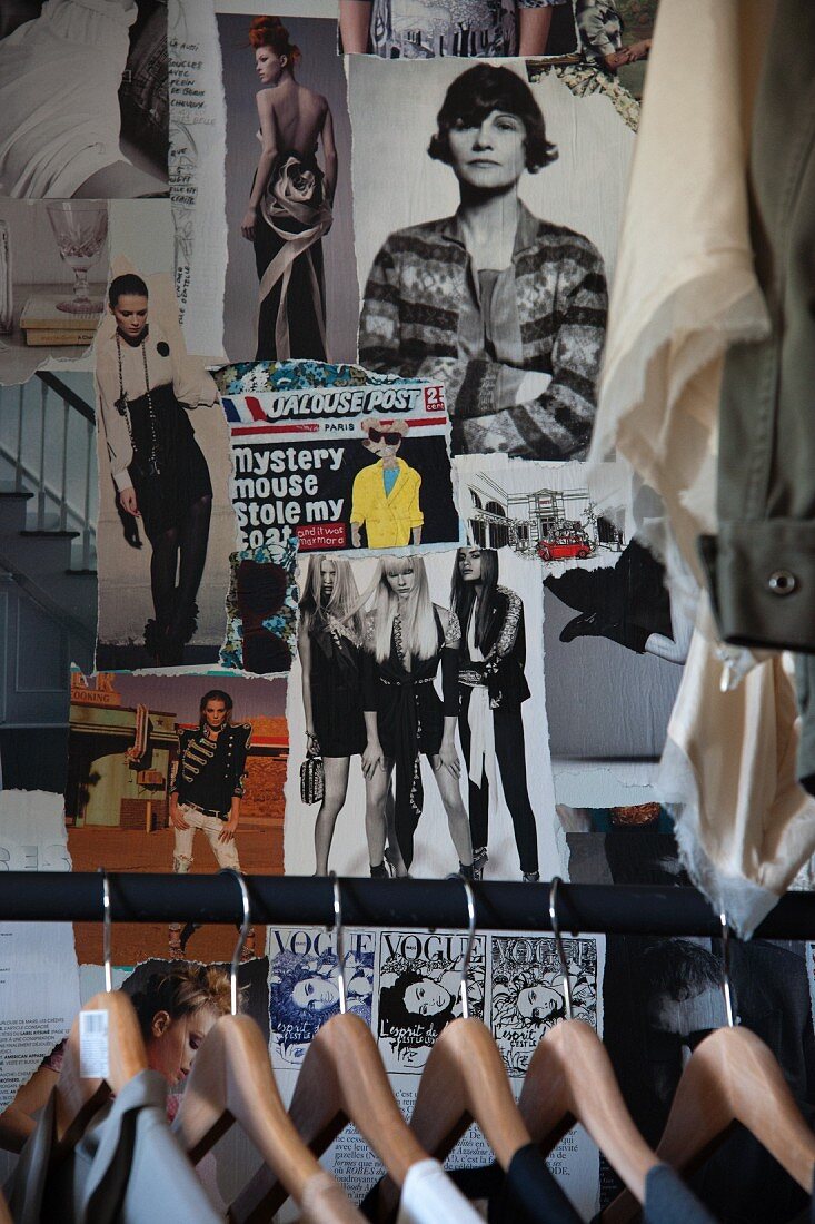 Wooden coathangers on clothes rail in front of wall decorated with photos cut from magazines