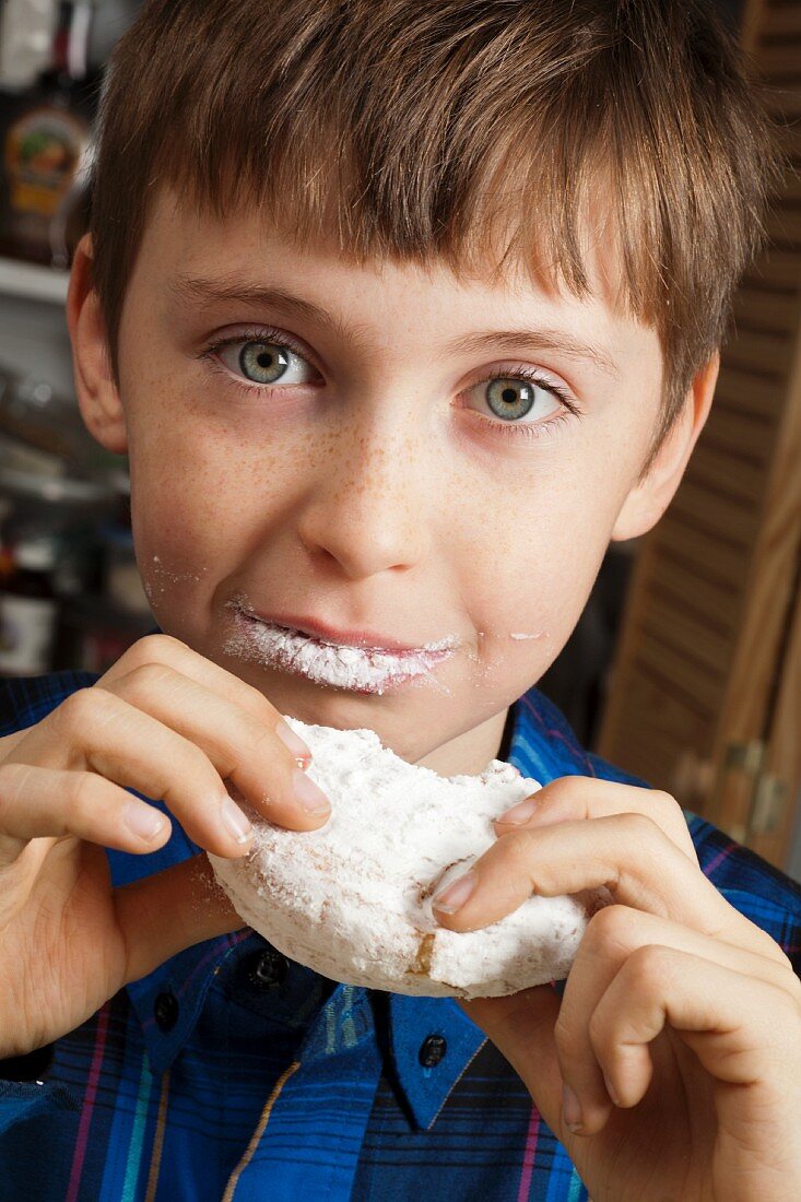 Junge isst Doughnut mit Puderzucker und Marmeladenfüllung