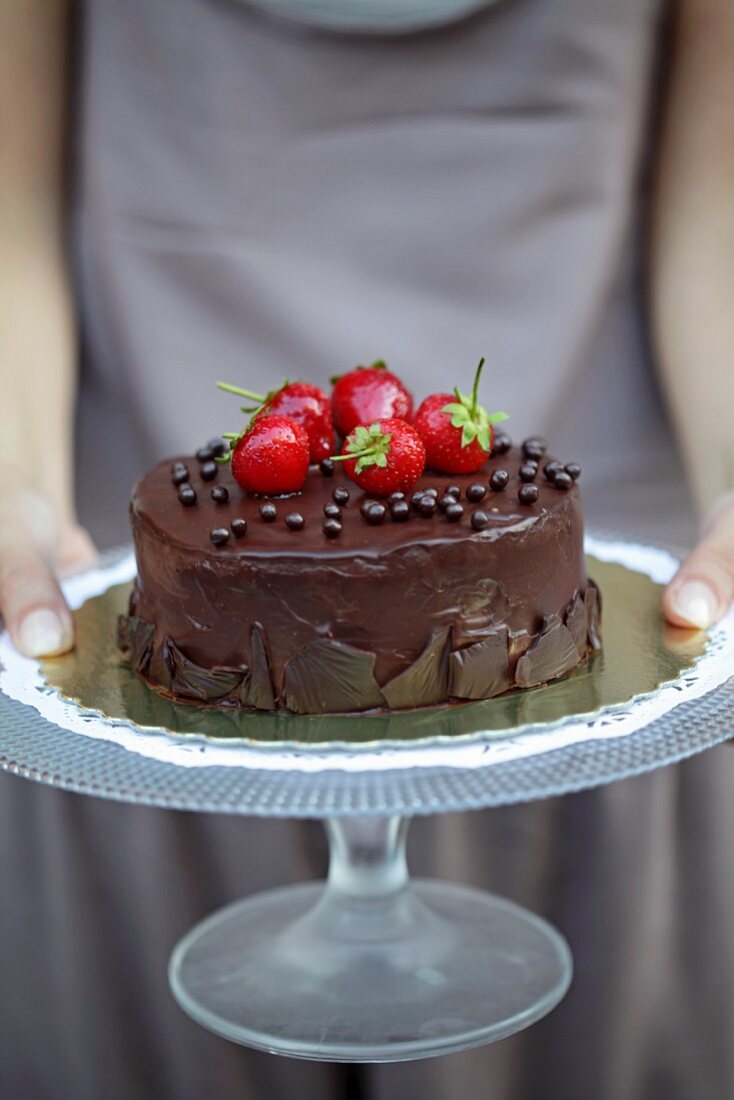 A woman holding a chocolate cake topped with strawberries