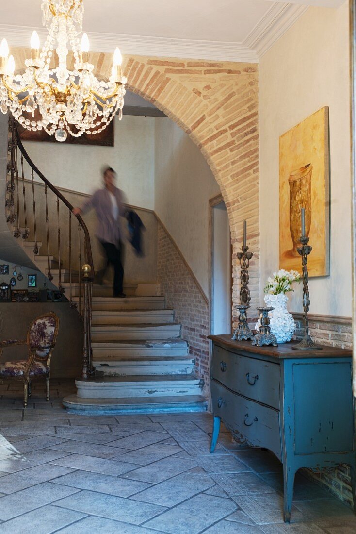 Wooden chest of drawers and chandelier in foyer with archway and staircase