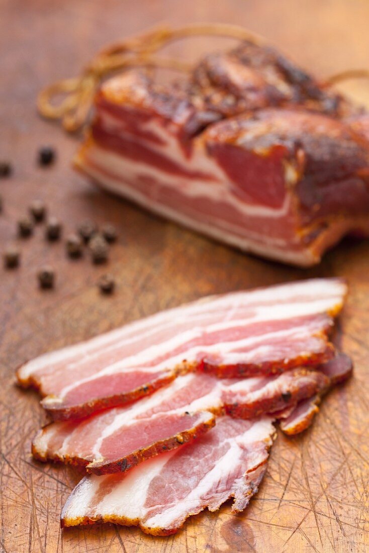 A piece of Tyrolean bacon and slices with peppercorns