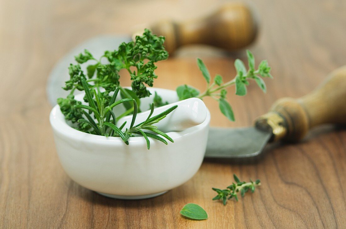 Parsley, oregano, rosemary in a mortar and a chopping knife