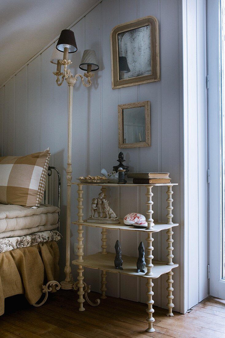 Collection of ornaments on flea-market shelves and old standard lamp with ornamental metal base next to sofa