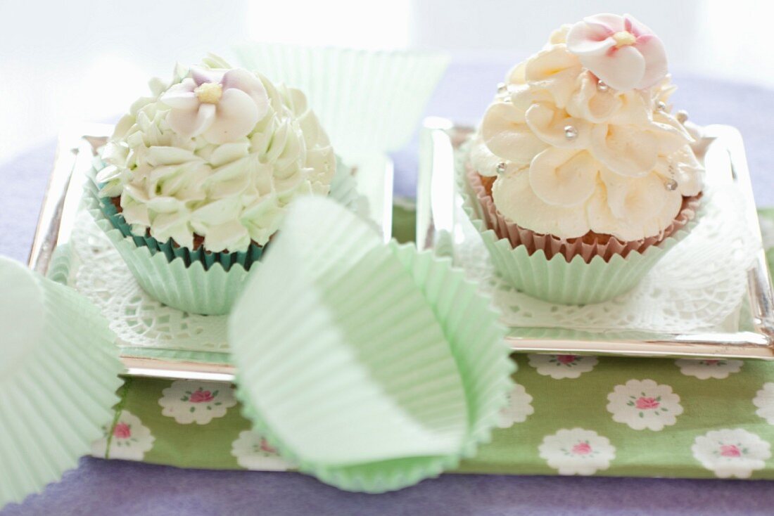 Two cupcakes topped with frosting on silver trays