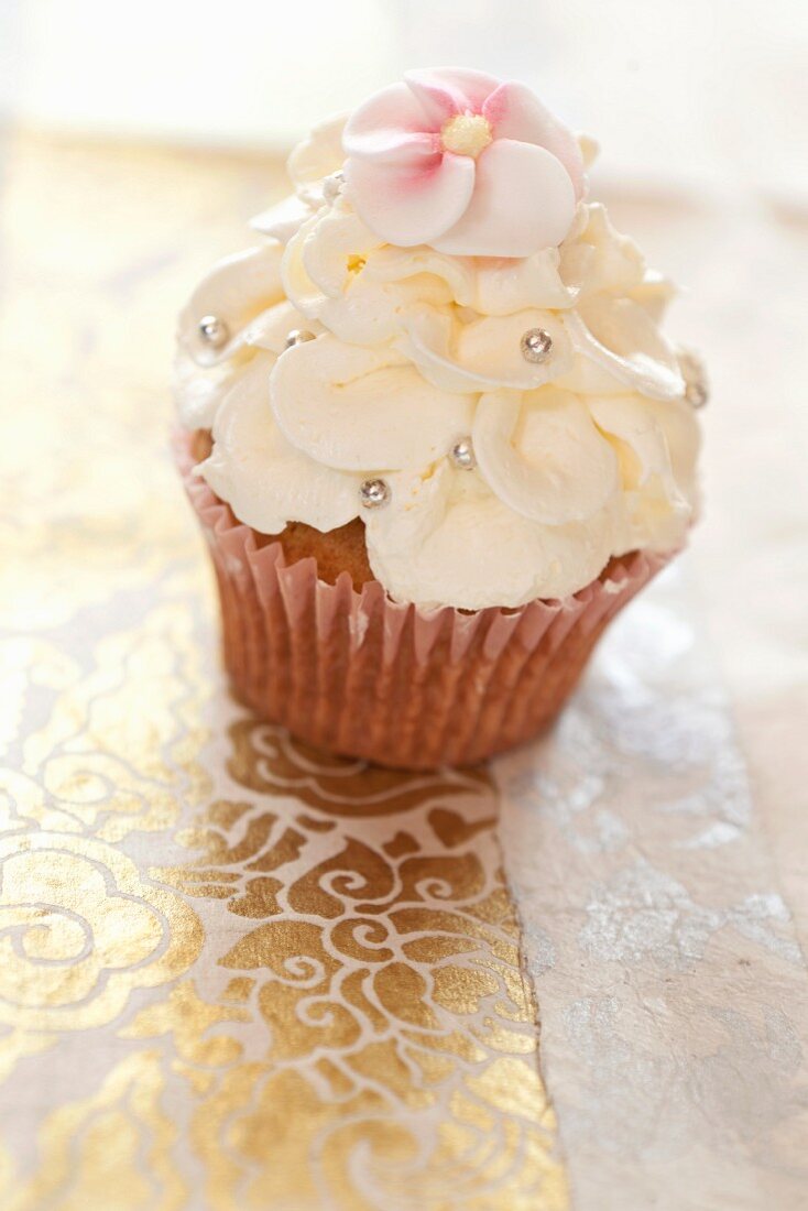 A cupcake topped with frosting, sugar flowers and sugar balls