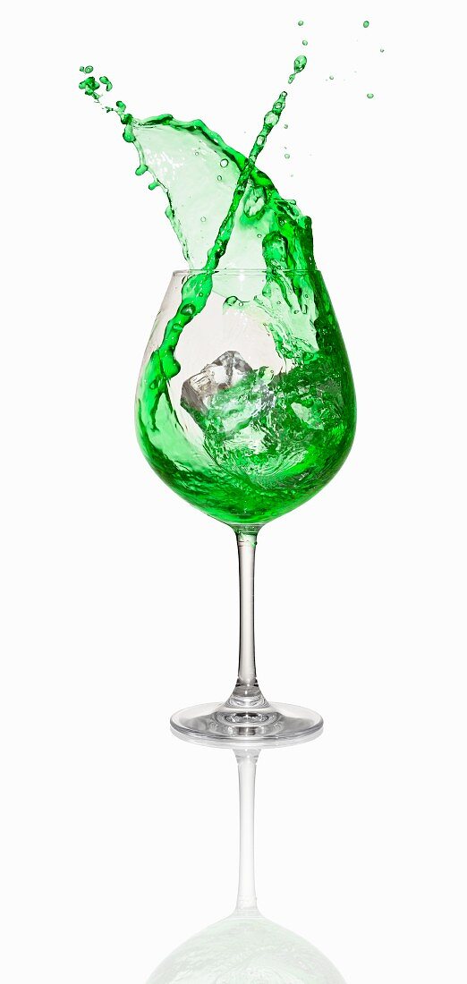 An ice cube falling into a green cocktail