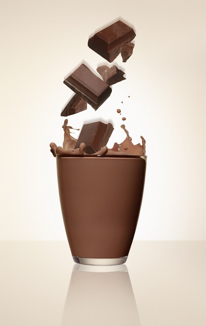 Schokoladenstücke fallen in ein Glas Kakao