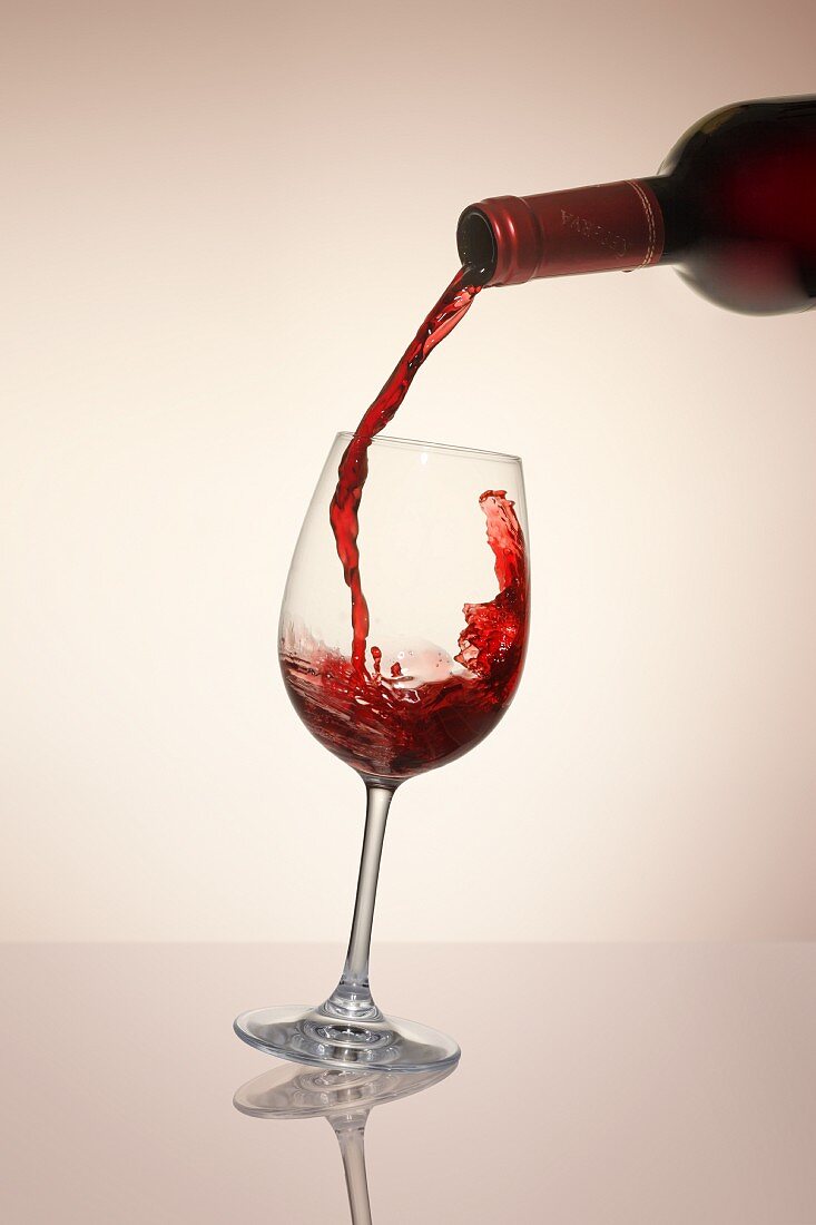 Rotwein aus Flasche in ein Glas gießen