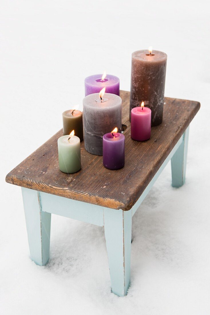 A variety of colourful candles on old footstool in snow